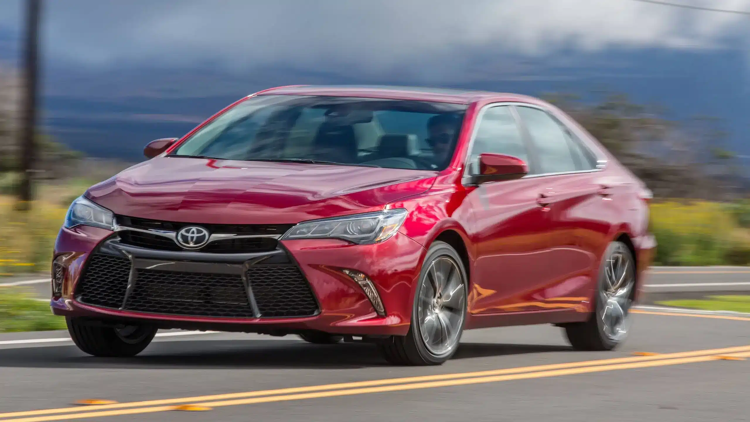 Red Toyota Camry driving on a scenic road, showcasing reliability and performance in used car options.