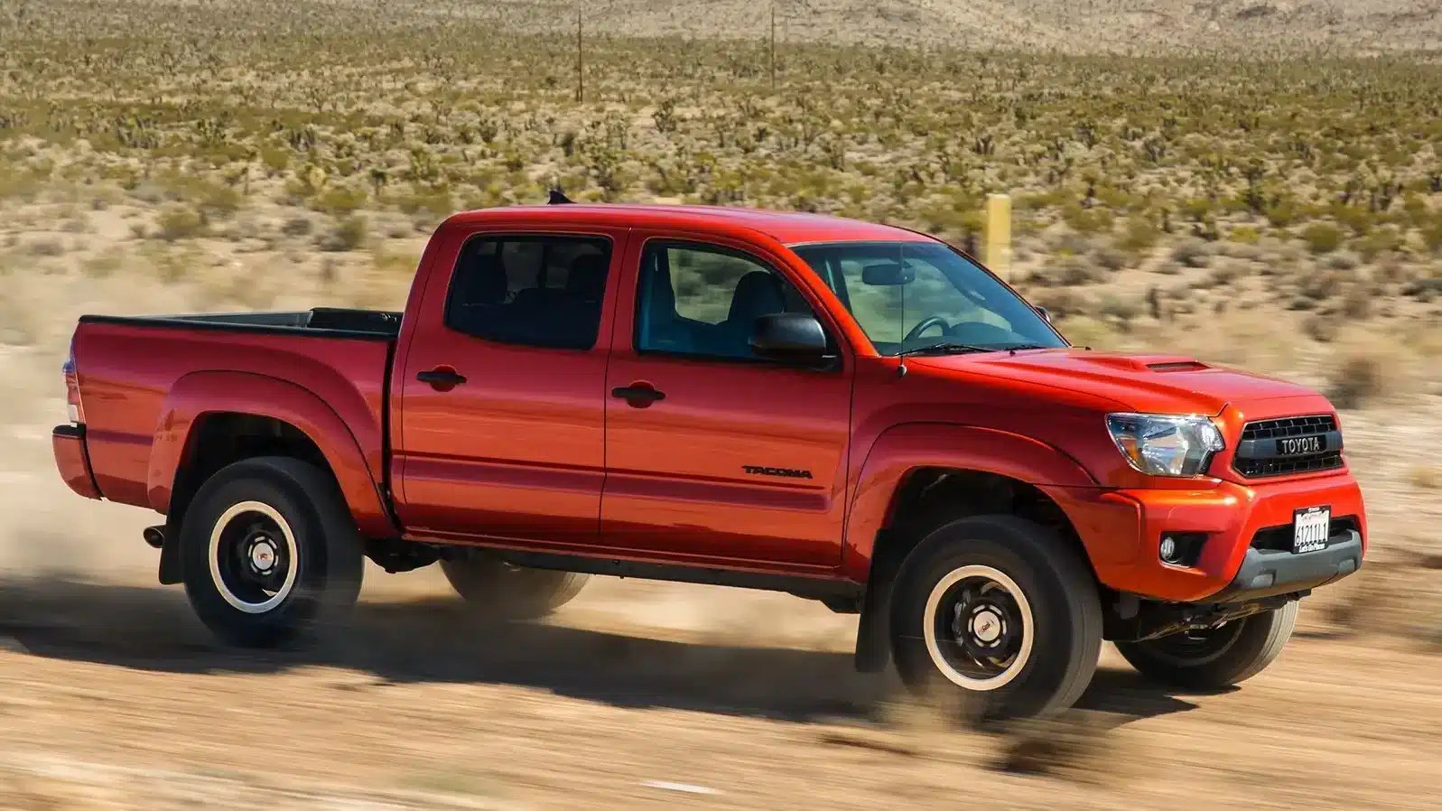 A bold red Toyota Tacoma pickup truck driving off-road, famous for its ruggedness and long-term reliability.