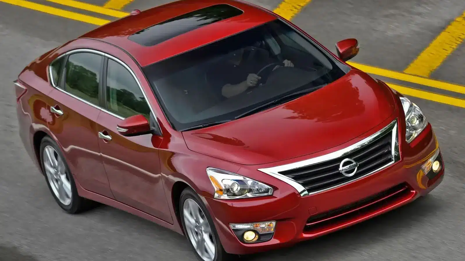 A red Nissan Altima sedan driving down a city road, highlighting its sleek design and reputation for dependability.