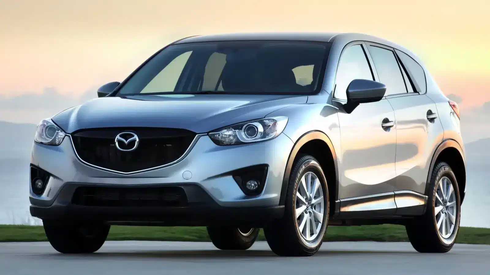 Front view of a silver Mazda CX-5 SUV parked outdoors at sunset, showcasing its sleek design and reliability.