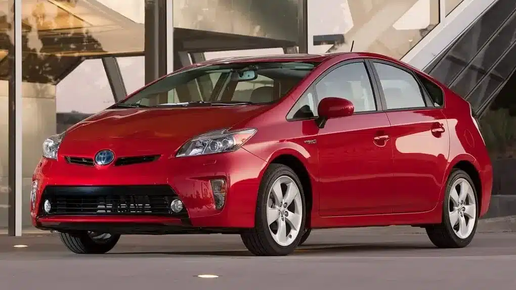 A shiny red Toyota Prius hybrid sedan parked in front of a modern building, highlighting its eco-friendly and fuel-efficient reputation.