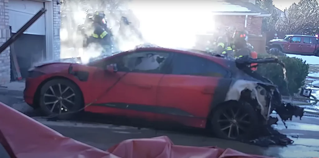 Firefighters extinguishing a fire on a Jaguar I-PACE, highlighting the fire risks associated with electric vehicles during charging, as discussed in dealership safety and insurance guidelines.