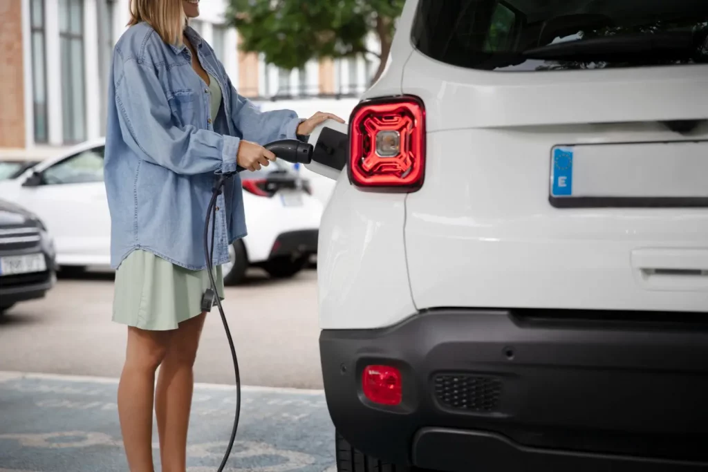 Woman charging her electric vehicle at a public station, illustrating the growth of EV infrastructure funded by $521 million in U.S. grants.