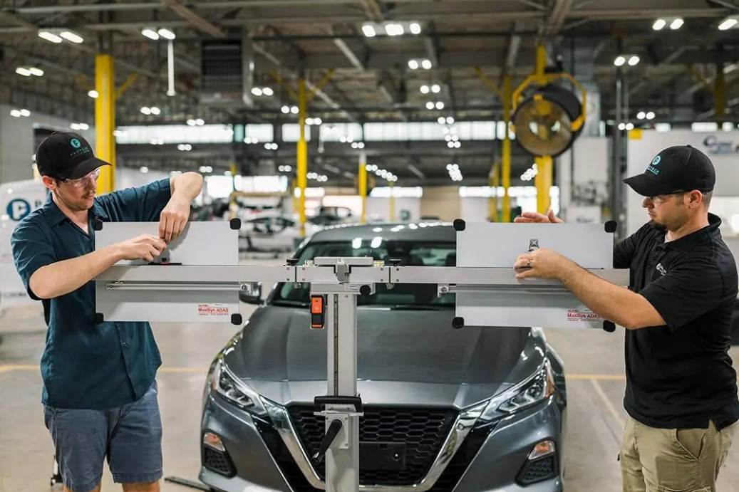 Two technicians using a MaxSys ADAS calibration tool in front of a Nissan after collision repair, illustrating post-accident sensor recalibration. | Diminished Value of Georgia, Car Appraisals for Insurance Claims