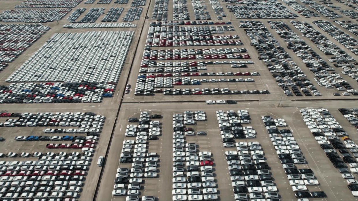 Aerial View of New Car Inventory Lot Amid Rising Incentives – Diminished Value of Georgia, Car Appraisals for Insurance Claims Aerial view of a massive car lot with vehicles parked in rows forming large letters on the ground. | Diminished Value of Georgia, Car Appraisals for Insurance Claims