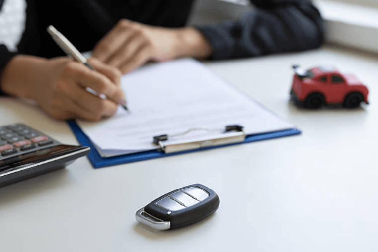 diminished-value-claim-without-lawyer-georgia – Diminished Value of Georgia, Car Appraisals for Insurance Claims Person signs a form on a clipboard at a clean desk, with a calculator and a small red toy car nearby. | Diminished Value of Georgia, Car Appraisals for Insurance Claims