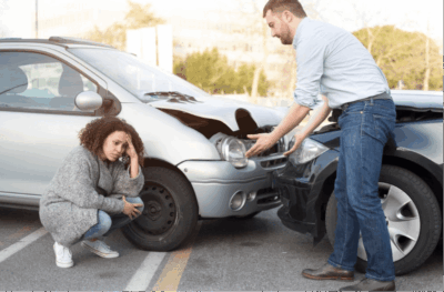 Two people assessing car collision damage in a parking lot in Georgia – Diminished Value of Georgia, Car Appraisals for Insurance Claims Woman crouching beside damaged car while man points to front-end collision damage in a parking lot, illustrating a parking lot accident diminished value claim in Georgia | Diminished Value of Georgia, Car Appraisals for Insurance Claims