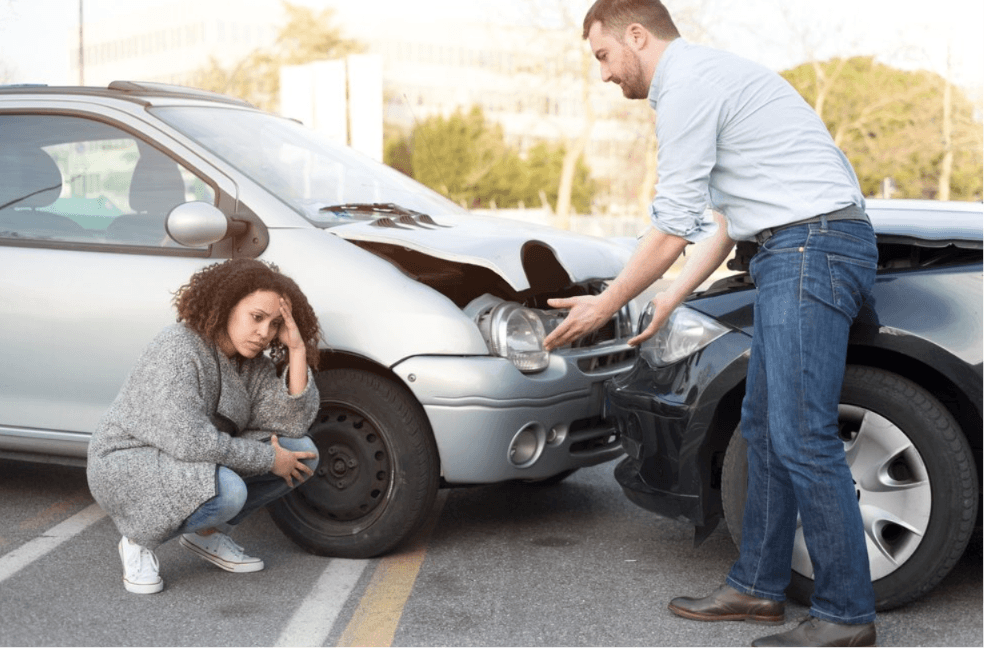 Two people assessing car collision damage in a parking lot in Georgia – Diminished Value of Georgia, Car Appraisals for Insurance Claims Woman crouching beside damaged car while man points to front-end collision damage in a parking lot, illustrating a parking lot accident diminished value claim in Georgia | Diminished Value of Georgia, Car Appraisals for Insurance Claims