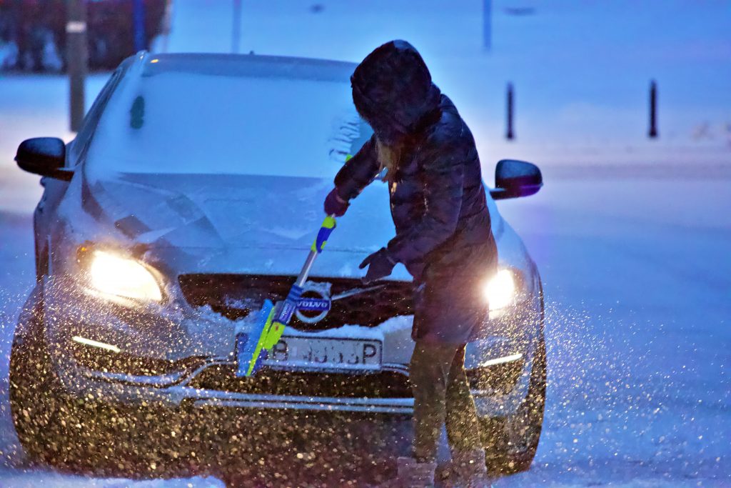 women cleaning the front of the car from snow